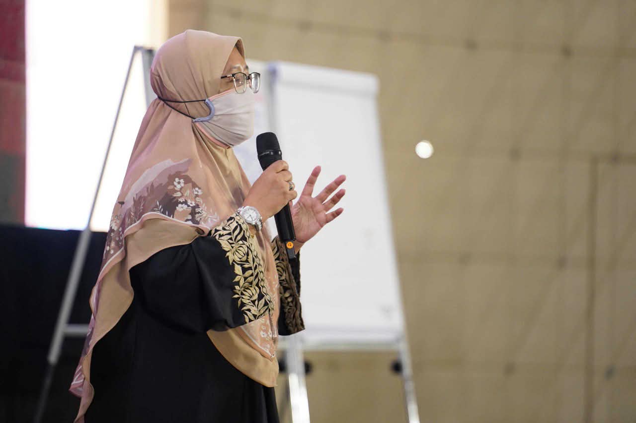 Coach Ida speaking on stage with a microphone at a global seminar